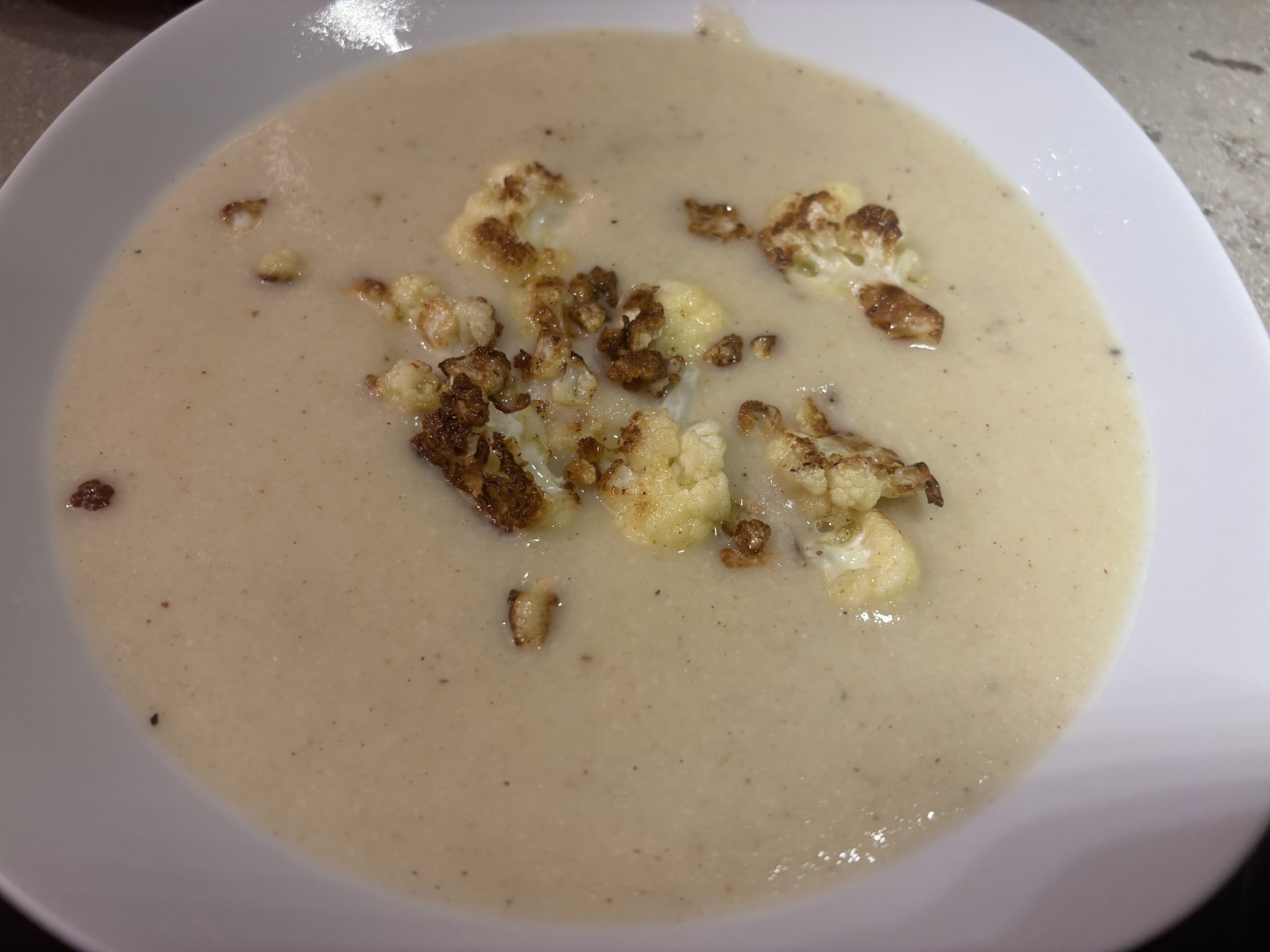 Blumenkohlcremesuppe im Teller mit gerösteten Blumenkohlstücken und Schnittlauch