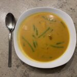 Ein Teller Bombay‑Masala‑Suppe mit Lachs, Bohnen und Mais, cremig angerichtet und aromatisch gewürzt.