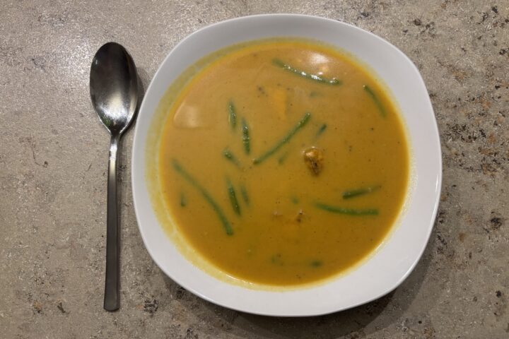 Ein Teller Bombay‑Masala‑Suppe mit Lachs, Bohnen und Mais, cremig angerichtet und aromatisch gewürzt.