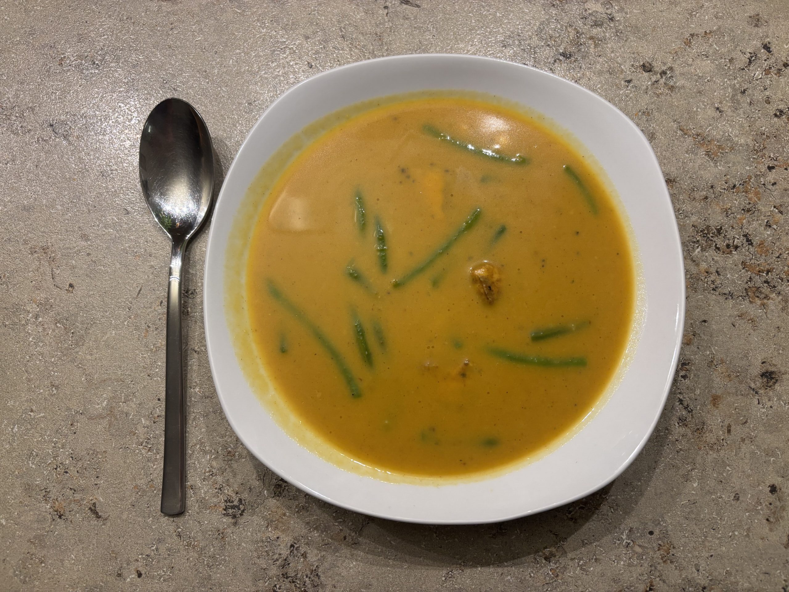 Ein Teller Bombay‑Masala‑Suppe mit Lachs, Bohnen und Mais, cremig angerichtet und aromatisch gewürzt.