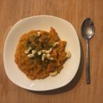 Ein Teller cremiges Linsen‑Dal mit Kürbis, serviert mit Kräutern und warmen Gewürzen.