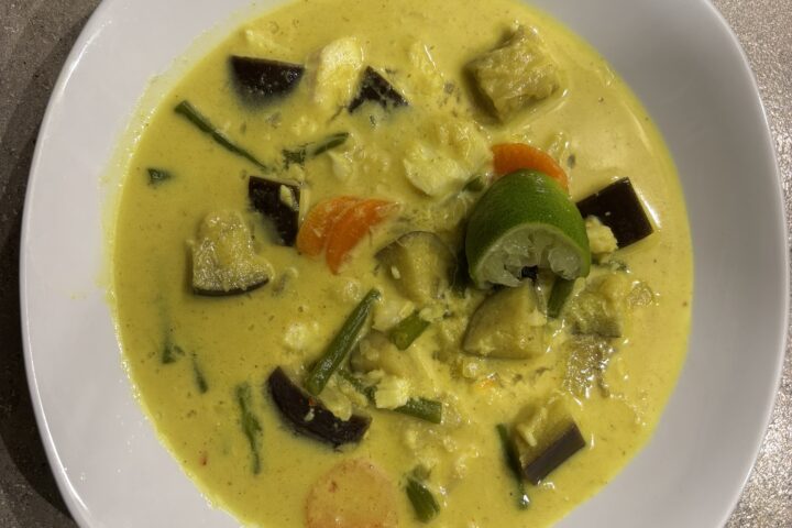 Ein Teller Weißfisch‑Curry mit cremiger Sauce, Gemüse und frischen Kräutern.